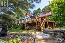Wood-sided multi-level residence featuring a red gable roof and a prominent elevated wood deck with railing - 