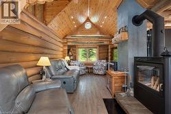 Vaulted wood-paneled ceilings with recessed lighting, exposed log walls, a wood-finish floor, and a built-in wood-burning fireplace with a stone hearth - 