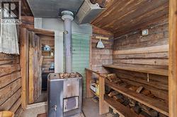 Wood-paneled interior featuring a wood-burning stove with a stone top, integrated wood storage, exposed wood beam ceiling, and a wall-mounted thermometer - 