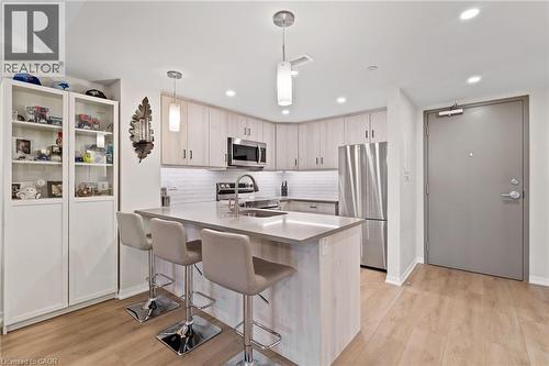 Kitchen with a peninsula, stainless steel appliances, a kitchen breakfast bar, decorative light fixtures, and light wood-type flooring - 3998 Victoria Avenue Unit# 105, Lincoln, ON - Indoor Photo Showing Kitchen