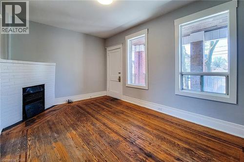 Room featuring wood-finish flooring, a white-painted brick fireplace with an iron grate, and light grey walls - 254 Emerald Street N Unit# Upper, Hamilton, ON - Indoor Photo Showing Other Room