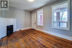 Room featuring wood-finish flooring, a white-painted brick fireplace with an iron grate, and light grey walls - 