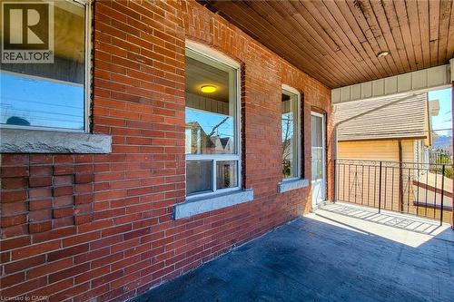 Brick exterior with white window trim and stone sills, featuring a covered porch with a wood plank ceiling, concrete flooring, and an ornate metal railing - 254 Emerald Street N Unit# Upper, Hamilton, ON - Outdoor With Exterior