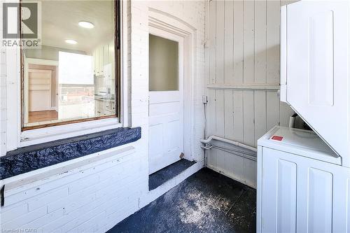 Outdoor laundry area with a stacked washer and dryer unit, white painted paneling, and an exterior window providing a glimpse into an interior room with white cabinetry - 254 Emerald Street N Unit# Upper, Hamilton, ON - Indoor