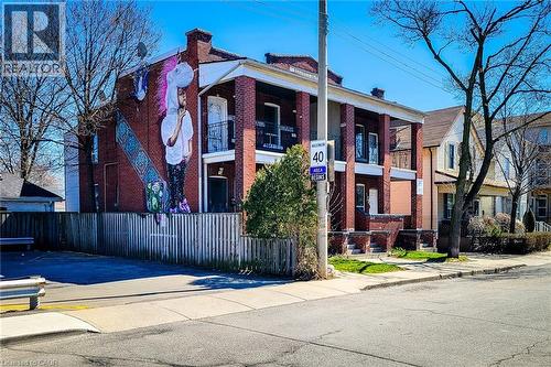 Brick exterior featuring a multi-story mural, two elevated balconies with black railings, and a fenced side yard - 254 Emerald Street N Unit# Upper, Hamilton, ON - Outdoor With Facade
