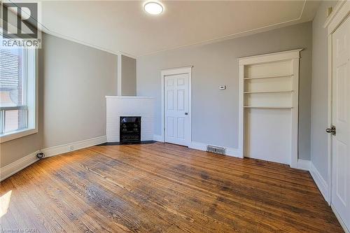Spacious room featuring wood-finish flooring, a white-painted brick fireplace with a black grate, a built-in shelving unit, and a white trim package - 254 Emerald Street N Unit# Upper, Hamilton, ON - Indoor With Fireplace