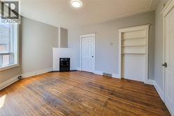 Spacious room featuring wood-finish flooring, a white-painted brick fireplace with a black grate, a built-in shelving unit, and a white trim package - 