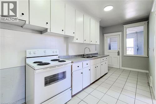 Kitchen featuring white tile flooring, white cabinetry with black hardware, a dual basin stainless steel sink, and a white electric range - 254 Emerald Street N Unit# Upper, Hamilton, ON - Indoor Photo Showing Kitchen With Double Sink