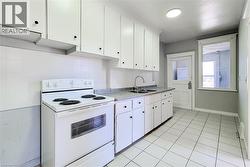 Kitchen featuring white tile flooring, white cabinetry with black hardware, a dual basin stainless steel sink, and a white electric range - 