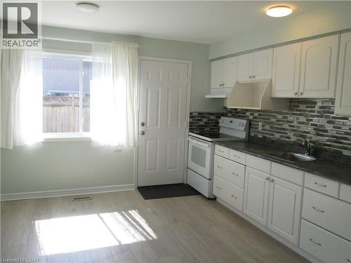 Kitchen featuring light wood-finish flooring, white cabinetry with silver hardware, a dark countertop, and a mosaic tile backsplash - 648 Francis Road, Burlington, ON - Indoor Photo Showing Kitchen