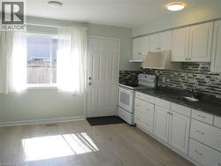 Kitchen featuring light wood-finish flooring, white cabinetry with silver hardware, a dark countertop, and a mosaic tile backsplash - 