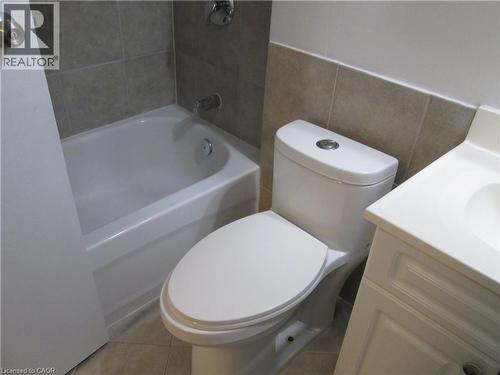 Bathroom featuring a white bathtub, tiled shower surround, commode with top-mounted flush button, and a white vanity with integrated sink - 648 Francis Road, Burlington, ON - Indoor Photo Showing Bathroom
