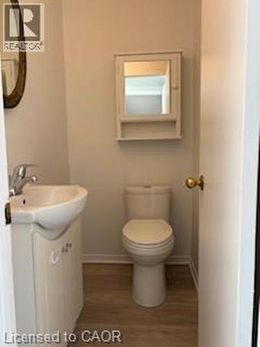 Compact bathroom featuring a wall-mounted sink with integrated storage, a standard toilet, and wood-finish flooring - 648 Francis Road, Burlington, ON - Indoor Photo Showing Bathroom