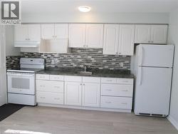 Kitchen featuring white cabinetry, a mosaic tile backsplash, dark-toned countertops, wood-finish flooring, and white appliances - 