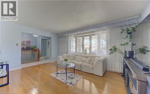 Bright living area featuring wood-finish flooring, a large bay window, light blue painted walls, and a decorative ceiling fixture visible in the adjacent hallway - 170 Martinglen Crescent, Kitchener, ON - Indoor Photo Showing Living Room