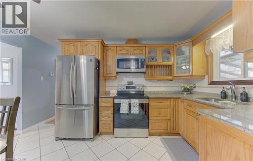 Kitchen featuring wood cabinetry, stainless steel appliances, white tile flooring, granite-look countertops, and a tile backsplash - 170 Martinglen Crescent, Kitchener, ON - Indoor Photo Showing Kitchen With Double Sink
