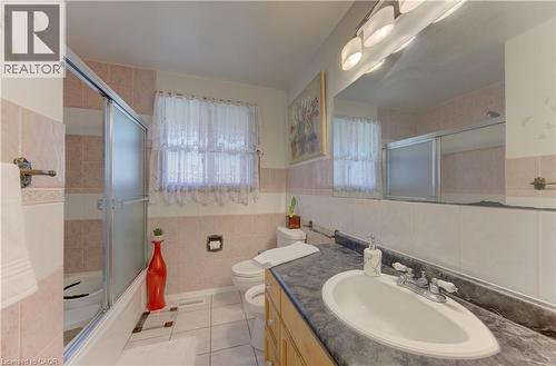 Bathroom featuring a shower enclosure with sliding frosted glass doors, a window with lace curtains, and a vanity with an integrated sink and dark countertop - 170 Martinglen Crescent, Kitchener, ON - Indoor Photo Showing Bathroom