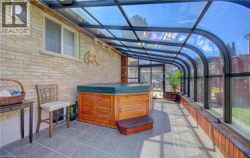 Sunroom featuring a curved glass ceiling, wood-encased hot tub, tiled flooring, light brick wall, and clear glass panels - 170 Martinglen Crescent, Kitchener, ON - Outdoor With Exterior