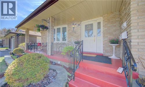 Brick exterior featuring a covered porch with a red-painted concrete surface, decorative wrought iron railing, and a white entrance door with sidelights - 170 Martinglen Crescent, Kitchener, ON - Outdoor