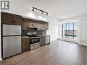 Open-concept living space featuring a contemporary kitchen with stainless steel appliances, dark wood-finish cabinetry, and a subway tile backsplash - 4878 Powers Common Unit# 1108, Burlington, ON  - Indoor Photo Showing Kitchen With Stainless Steel Kitchen 