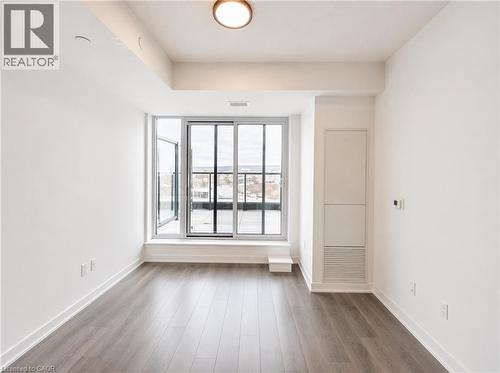 Spacious interior featuring wood-finish flooring, a contemporary ceiling light fixture, and a large sliding glass door opening to an outdoor balcony - 4878 Powers Common Unit# 1108, Burlington, ON - Indoor Photo Showing Other Room
