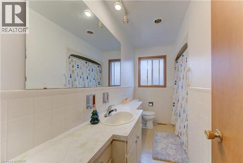 Bathroom featuring a single vanity with an integrated sink, a large wall-mounted mirror, white ceramic wall tiling, and a window with wood-finish trim - 98 Shea Crescent, Kitchener, ON - Indoor Photo Showing Bathroom