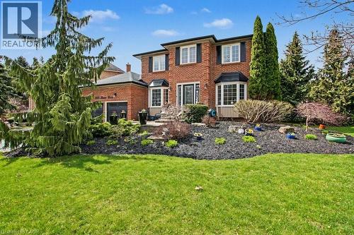 Brick facade residence featuring a two-car garage, bay window, landscaped front garden, mature trees, and a well-maintained lawn - 2324 Homer Drive, Burlington, ON - Outdoor