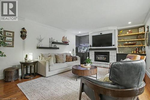Living area featuring wood-finish flooring, a white brick fireplace with a dark mantel, built-in shelving with recessed lighting, and crown molding - 2324 Homer Drive, Burlington, ON - Indoor Photo Showing Living Room With Fireplace