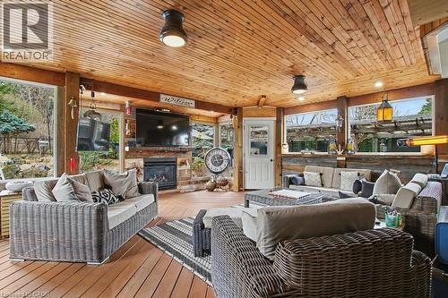 Spacious outdoor living area featuring a tongue-and-groove wood ceiling, wood-finish flooring, a built-in fireplace, and expansive windows - 2324 Homer Drive, Burlington, ON - Outdoor With Deck Patio Veranda