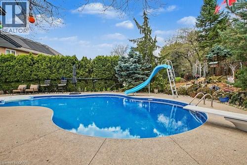 Curved inground pool with a concrete surround, featuring a diving board and a pool slide - 2324 Homer Drive, Burlington, ON - Outdoor With In Ground Pool With Backyard