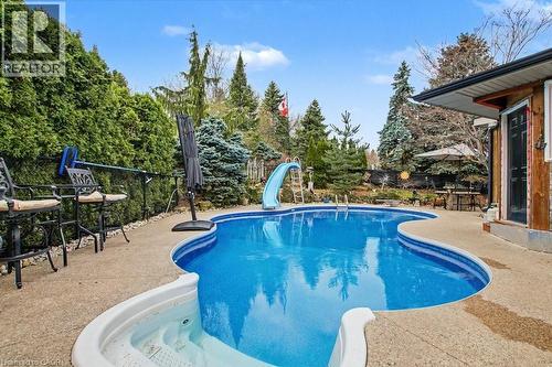 Rear yard featuring a freeform swimming pool with integrated spa and surrounding concrete patio - 2324 Homer Drive, Burlington, ON - Outdoor With In Ground Pool With Backyard