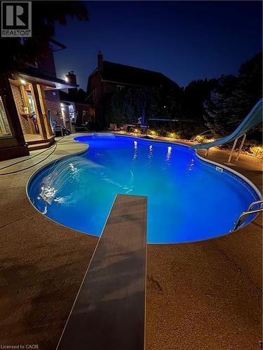 Freeform swimming pool with integrated diving board, waterslide, and surrounding textured concrete decking - 2324 Homer Drive, Burlington, ON - Outdoor With In Ground Pool With Backyard