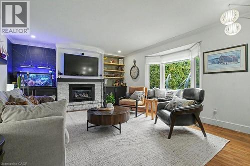 Living area featuring a white brick fireplace with a built-in media center, wood-finish flooring, and a bay window - 2324 Homer Drive, Burlington, ON - Indoor Photo Showing Living Room With Fireplace