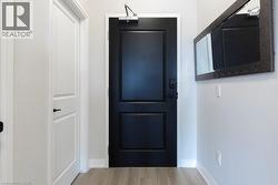 Modern entryway featuring a contrasting black paneled door with a door closer, light wood-finish flooring, and a textured rectangular mirror - 