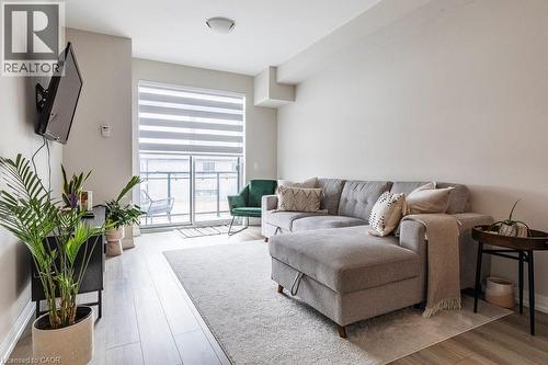 Spacious living area featuring light wood-finish flooring, a neutral wall palette, a built-in wall-mounted television, and a large sliding glass door with balcony access - 120 Springvalley Crescent Unit# 208, Hamilton, ON - Indoor Photo Showing Living Room