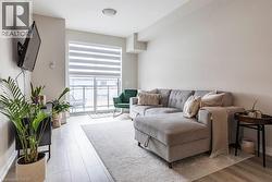 Spacious living area featuring light wood-finish flooring, a neutral wall palette, a built-in wall-mounted television, and a large sliding glass door with balcony access - 