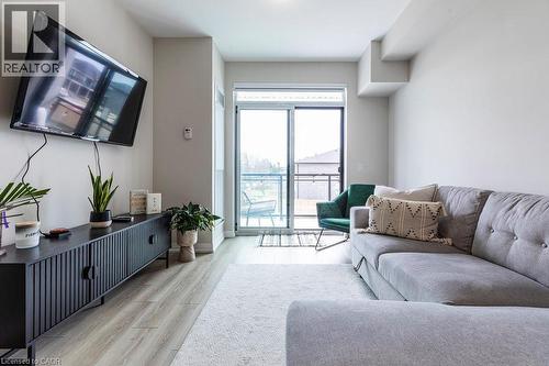 Living space featuring neutral wall tones, wood-finish flooring, a white area rug, and sliding glass doors opening to an outdoor area - 120 Springvalley Crescent Unit# 208, Hamilton, ON - Indoor Photo Showing Living Room