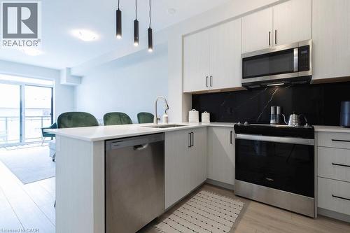 Modern kitchen featuring white cabinetry, light-toned countertops, and a striking dark backsplash - 120 Springvalley Crescent Unit# 208, Hamilton, ON - Indoor Photo Showing Kitchen With Upgraded Kitchen