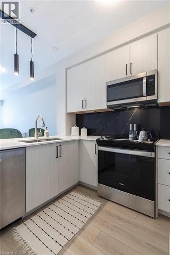 Modern kitchen featuring light wood-finish cabinetry, stainless steel appliances, and a black marble-look backsplash - 120 Springvalley Crescent Unit# 208, Hamilton, ON - Indoor Photo Showing Kitchen