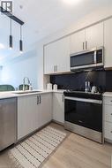 Modern kitchen featuring light wood-finish cabinetry, stainless steel appliances, and a black marble-look backsplash - 