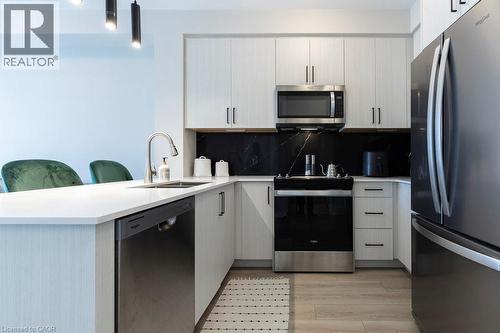 Modern kitchen featuring light wood-finish cabinetry, stainless steel appliances, white countertops, and a black backsplash with subtle veining - 120 Springvalley Crescent Unit# 208, Hamilton, ON - Indoor Photo Showing Kitchen With Stainless Steel Kitchen With Upgraded Kitchen
