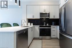 Modern kitchen featuring light wood-finish cabinetry, stainless steel appliances, white countertops, and a black backsplash with subtle veining - 
