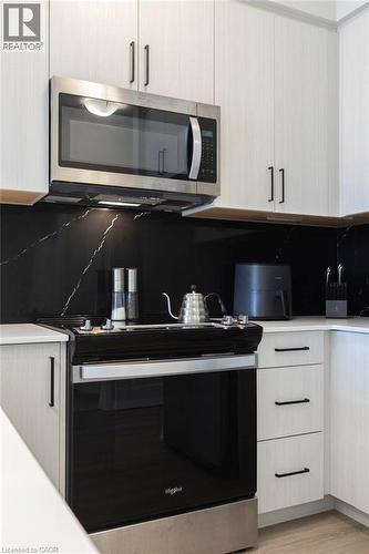Modern kitchen with light wood-finish cabinetry, black linear pulls, and a black marble-patterned backsplash - 120 Springvalley Crescent Unit# 208, Hamilton, ON - Indoor Photo Showing Kitchen