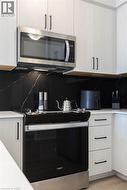 Modern kitchen with light wood-finish cabinetry, black linear pulls, and a black marble-patterned backsplash - 