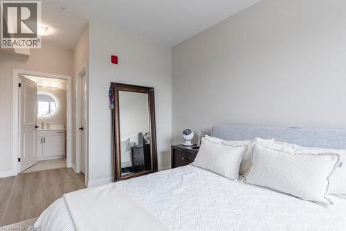 Bedroom with light wood-finish flooring and direct access to a bathroom featuring a circular backlit mirror, white vanity with storage, and a single basin sink - 120 Springvalley Crescent Unit# 208, Hamilton, ON - Indoor Photo Showing Bedroom
