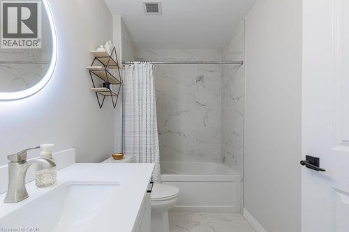 Contemporary bathroom featuring a combined tub and shower with marble-look wall tiling and a circular illuminated mirror - 120 Springvalley Crescent Unit# 208, Hamilton, ON - Indoor Photo Showing Bathroom