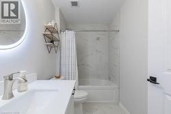 Contemporary bathroom featuring a combined tub and shower with marble-look wall tiling and a circular illuminated mirror - 