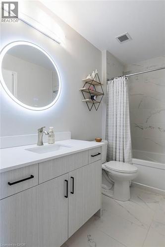 Modern bathroom featuring a single vanity with light wood-finish cabinetry and black hardware, a pristine white countertop with an integrated sink, and an illuminated circular mirror - 120 Springvalley Crescent Unit# 208, Hamilton, ON - Indoor Photo Showing Bathroom