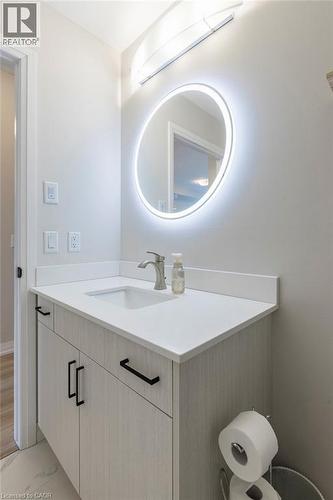 Bathroom vanity featuring a light wood-finish cabinet with black hardware, a pristine white countertop, and an undermount sink - 120 Springvalley Crescent Unit# 208, Hamilton, ON - Indoor Photo Showing Bathroom