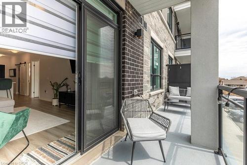 Private balcony featuring a concrete surface, black metal and glass railing, and brick and stone exterior finishes - 120 Springvalley Crescent Unit# 208, Hamilton, ON - Outdoor With Balcony With Exterior